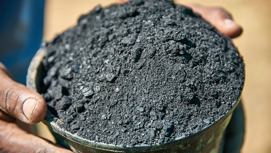 Hands holding a container of black biochar prepared for use as a soil amendment.