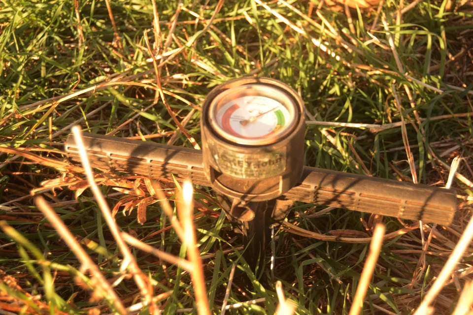 A soil probe with a round dial resting in grass.