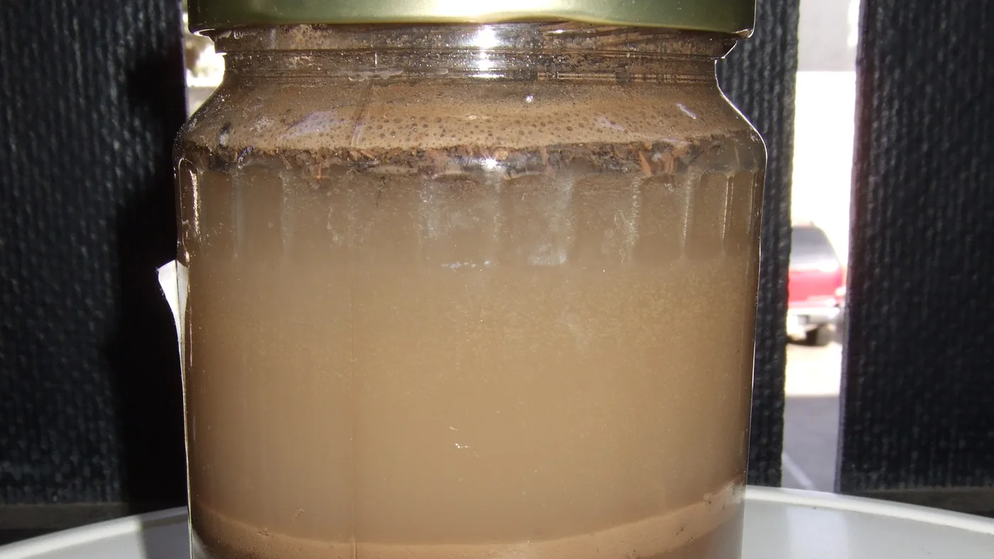 A clear jar with visible layers of settled garden soil.